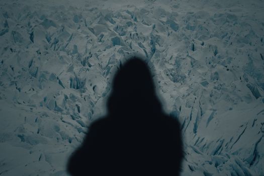 Mysterious hooded silhouette cast on an expansive icy glacier landscape under cool lighting.
