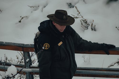 Man in a Winter Jacket and Hat Walking Outdoors in Snow 
