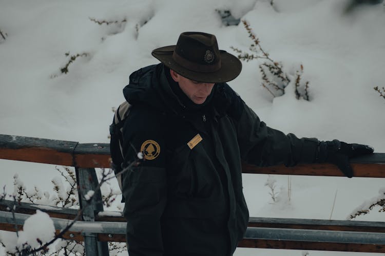 Man In A Winter Jacket And Hat Walking Outdoors In Snow 