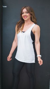 Fit woman smiling and posing indoors against a black background, showcasing her sporty outfit.