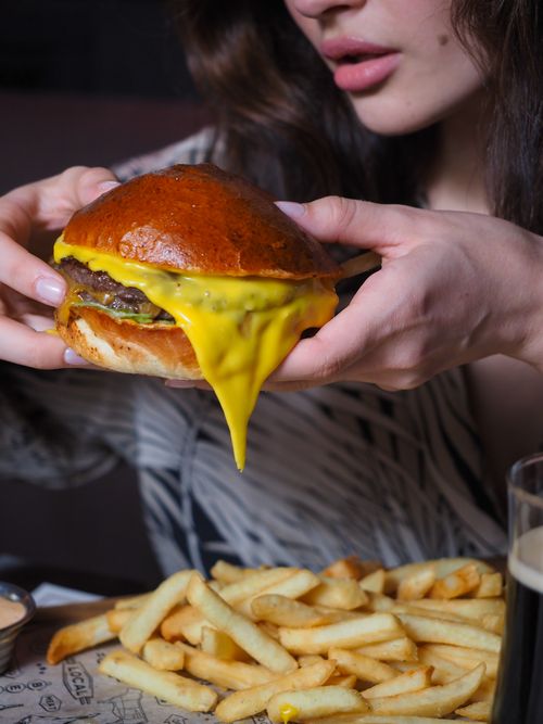 Free Close-up of a woman holding a melting cheeseburger with fries, perfect for fast food lovers. Stock Photo