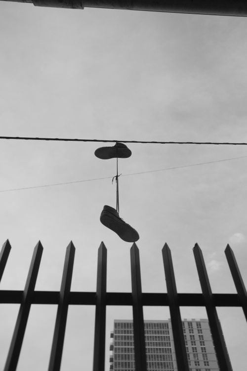 Free Monochrome view of sneakers hanging on a wire above a metal fence in an urban backdrop. Stock Photo