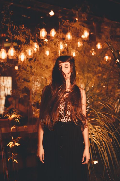 Free A serene woman with long hair illuminated by warm lights stands in a garden at night. Stock Photo