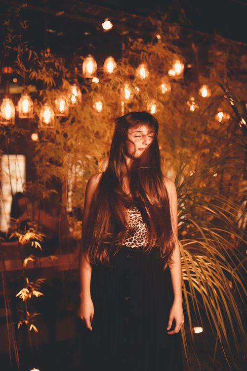 Free A woman with long hair poses gracefully in a warm, lantern-lit garden setting. Stock Photo