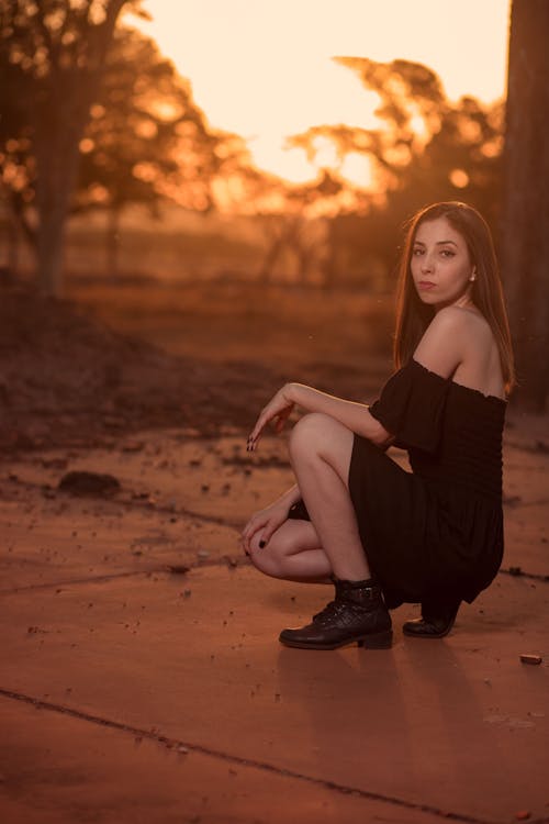 Woman in Black Dress Sitting on Concrete Pavement