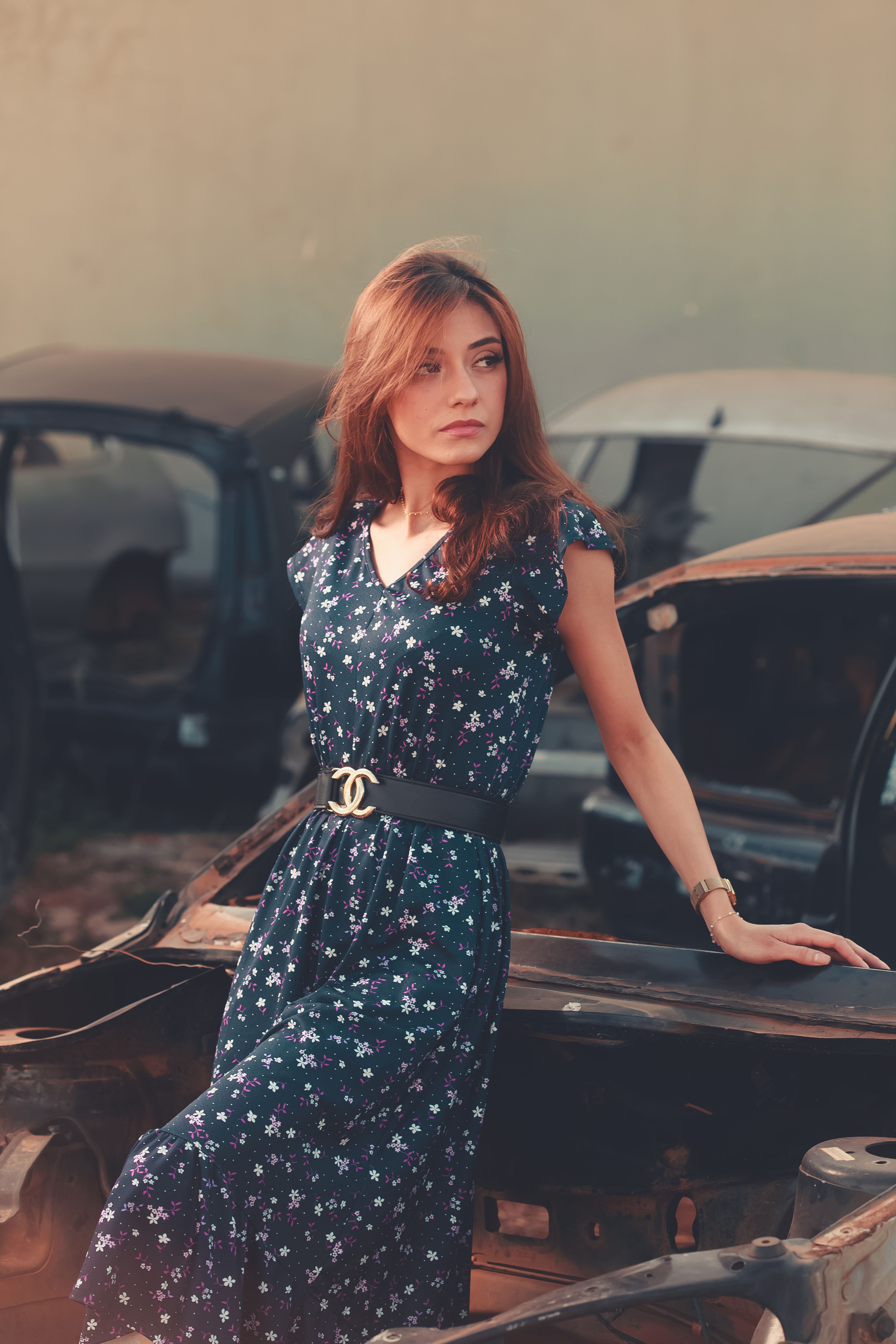 Mulher em vestido floral posando com confiança em um ferro-velho. A moda encontra a dureza urbana nesta sessão de fotos única.