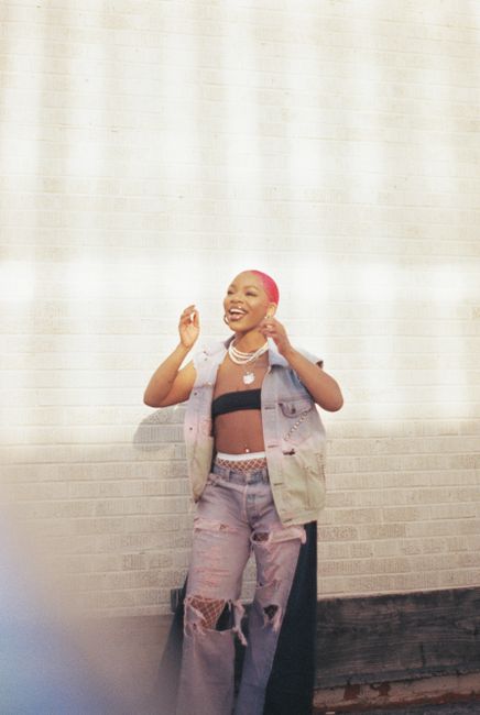 Stylish young woman with pink hair in vibrant denim against a bright wall, showcasing modern fashion.