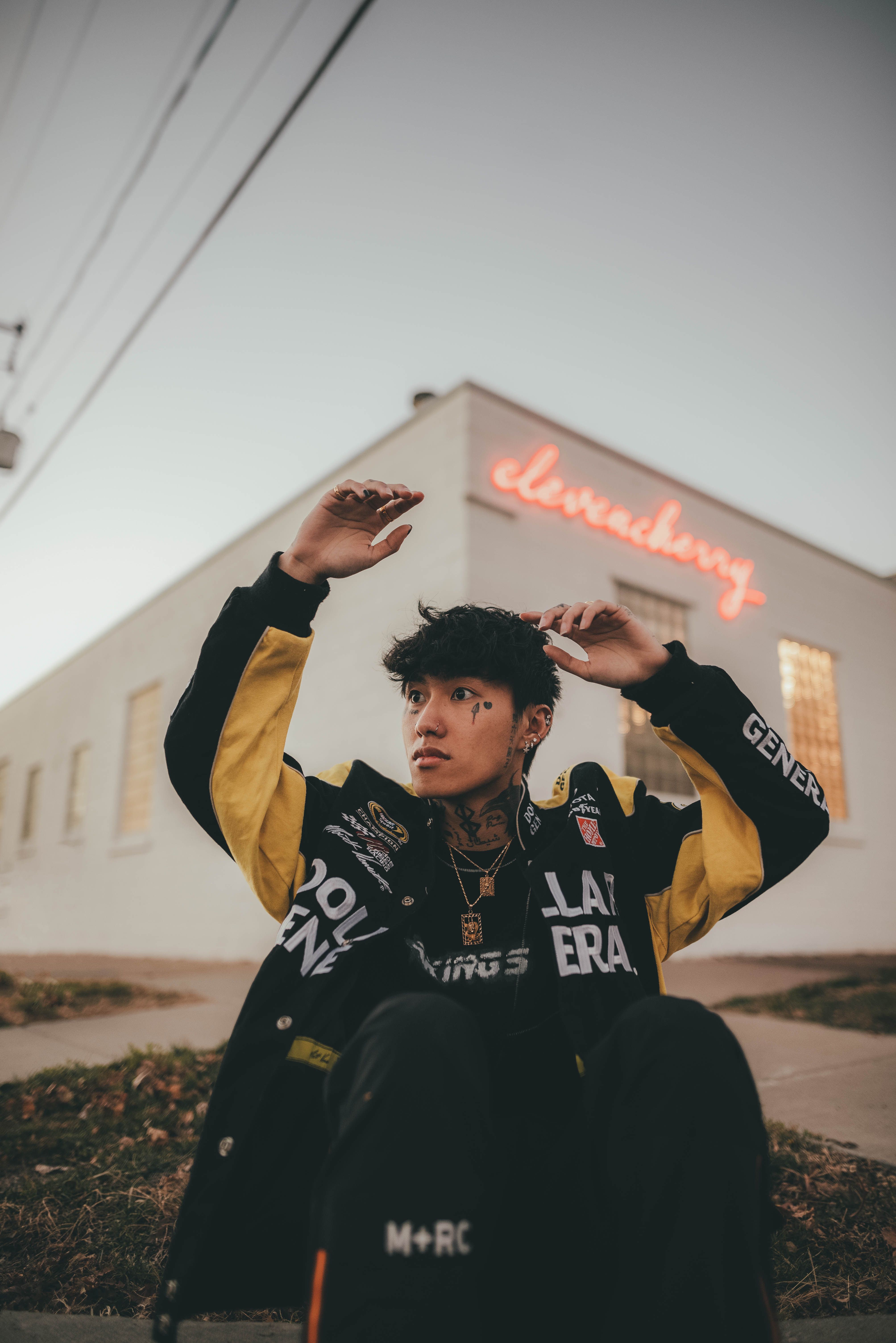 Stylish tattooed man posing in an urban street wearing trendy jacket with expressive gestures.
