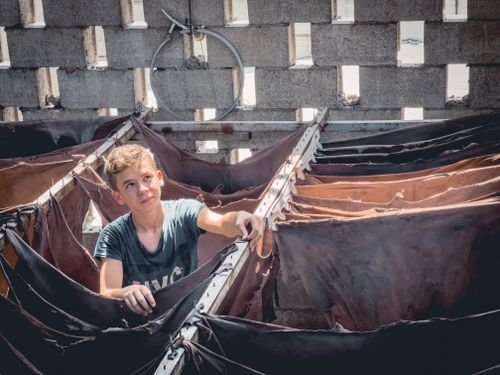 Free A young boy inspects leather hides in a sunlit workshop, showcasing traditional tanning. Stock Photo