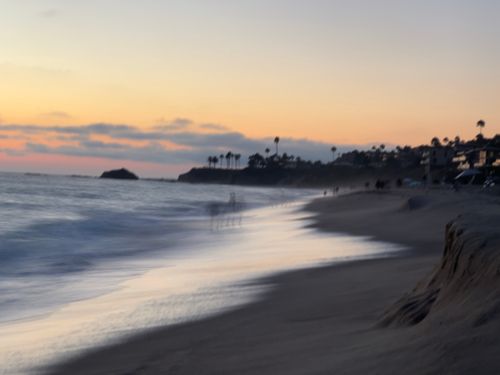 Free A tranquil beach scene at sunset with waves and silhouetted palm trees. Stock Photo