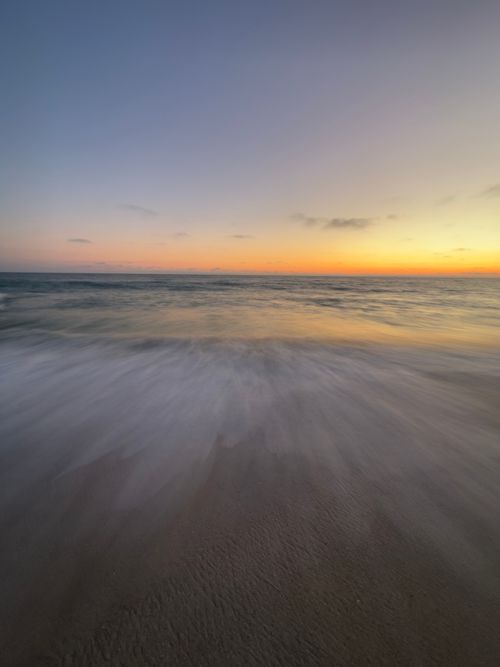 Free A tranquil ocean scene at sunset with waves gently washing onto the shore. Stock Photo