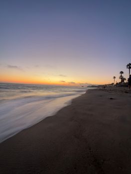 Tranquil beach scene capturing the serene sunset over the ocean, with waves gently lapping the shore.