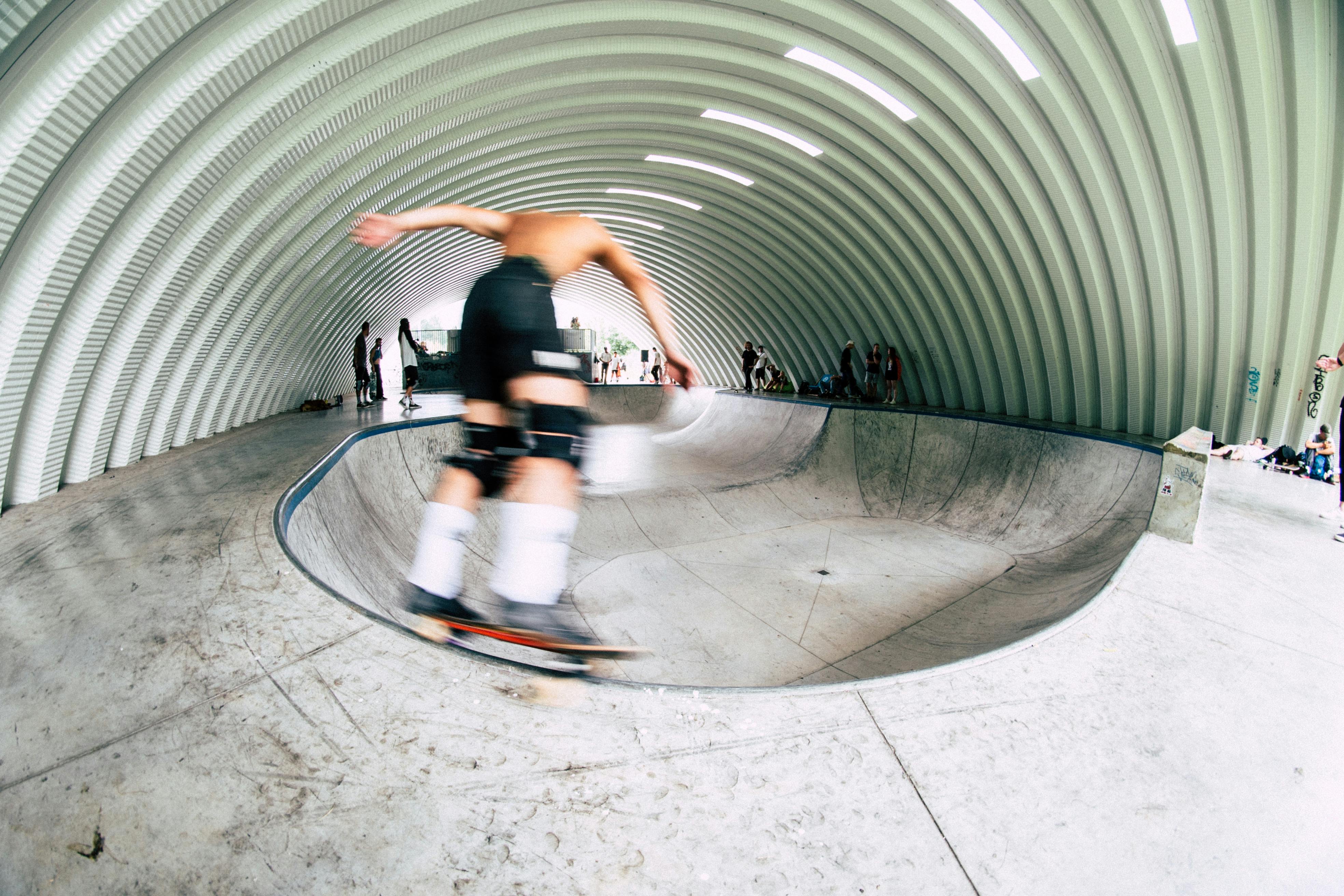 A skateboarder performs a trick in an indoor skatepark, showcasing motion and athleticism.