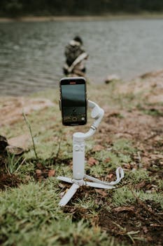 Close-up of a smartphone on a tripod recording by a serene lakeside, capturing natural beauty.