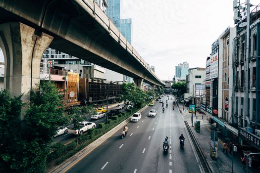 High angle view of a busy street in Bangkok with cars and motorcycles beneath an elevated train track, capturing urban life.