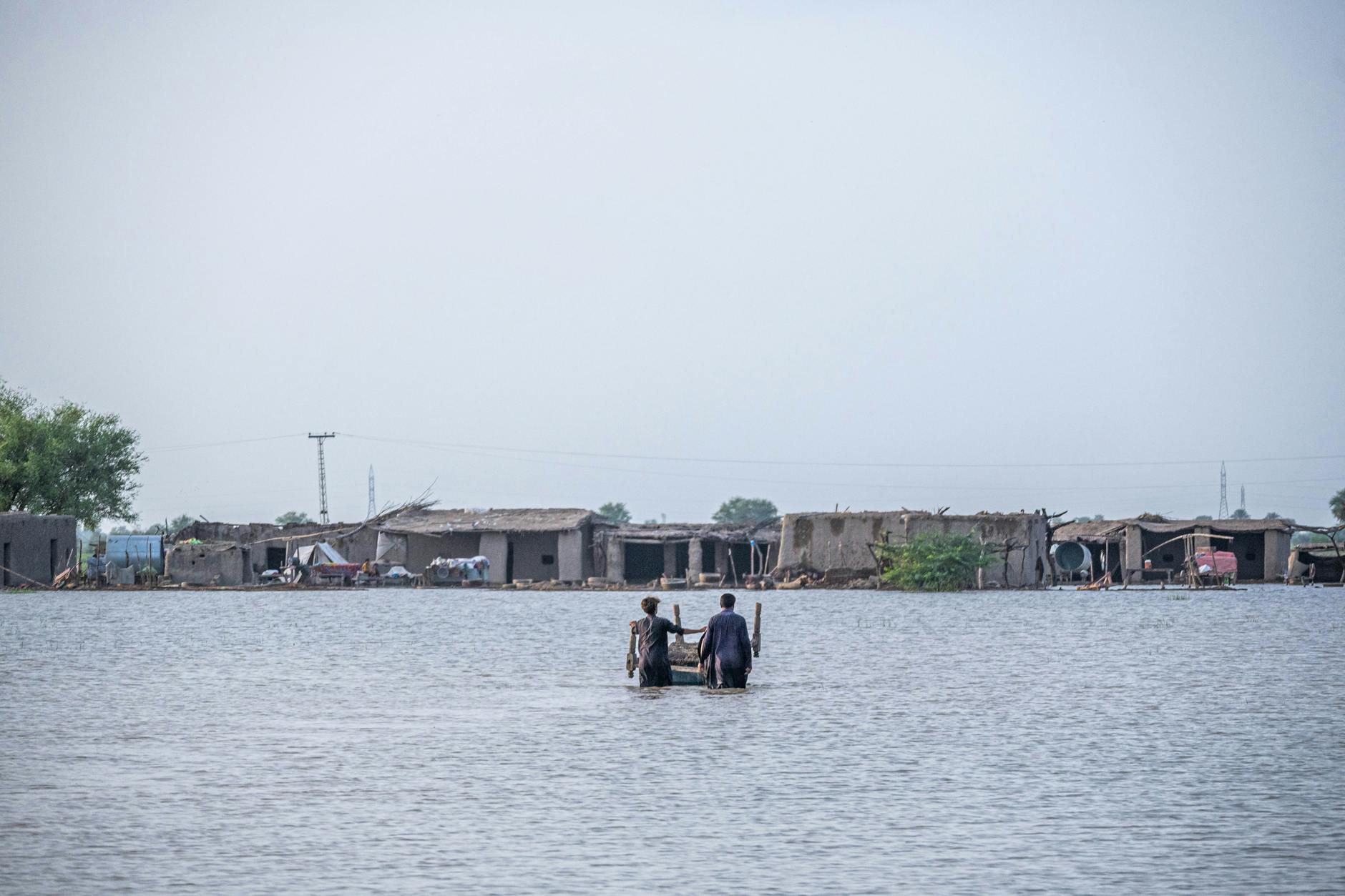 People wading through floodwaters in Gandakha City, highlighting the impact of the 2022 floods in Balochistan, Pakistan.