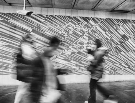 Black and white street scene featuring people with motion blur and abstract mural.