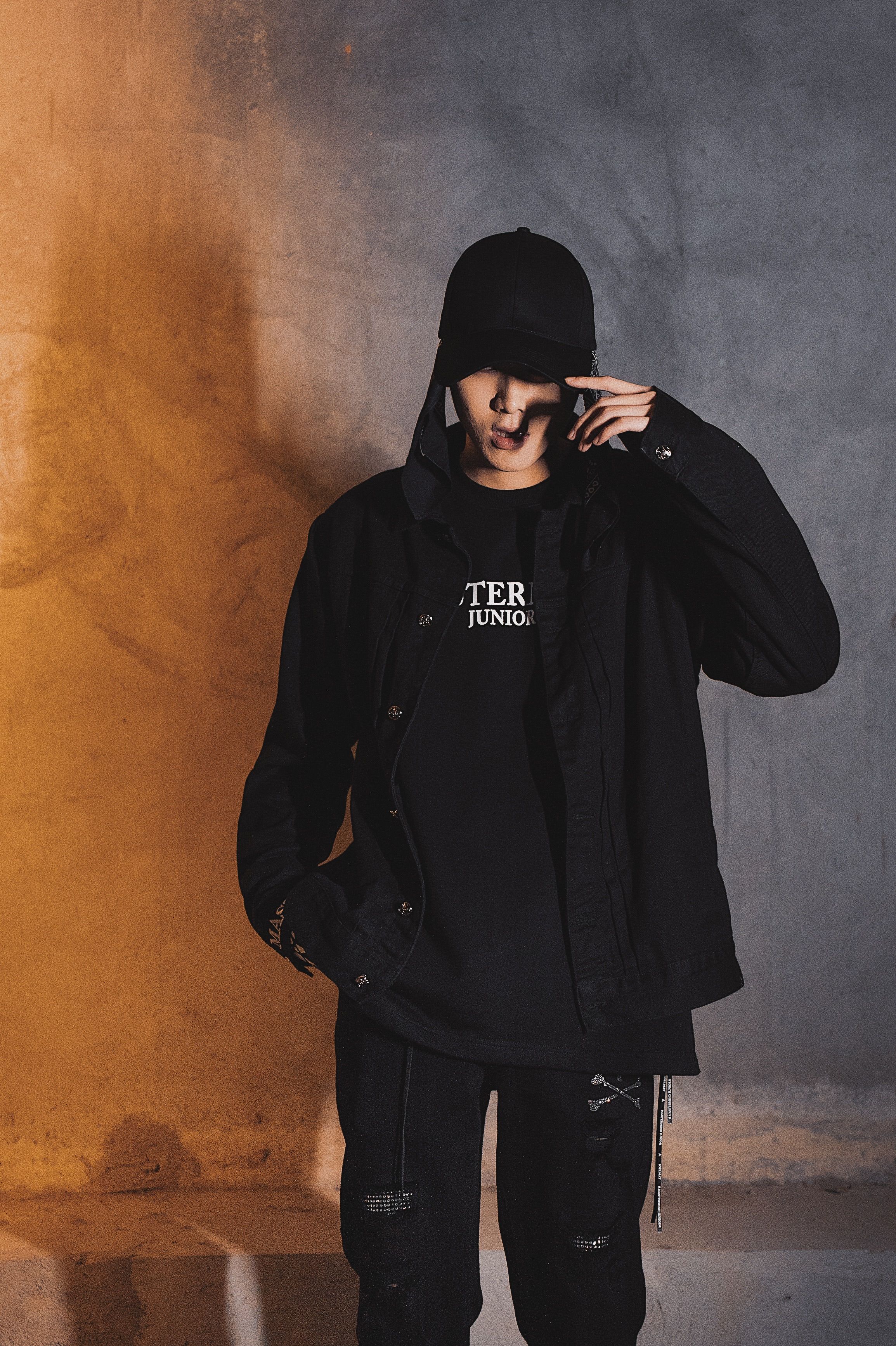 Captivating portrait of a young man in streetwear against a textured wall with moody lighting.