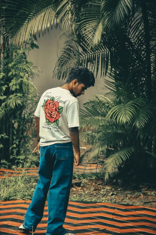 Free Casual young man standing amidst tropical plants in Kochi, India, wearing a rose-printed t-shirt. Stock Photo