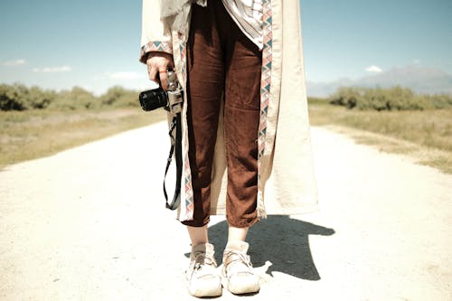 Person Standing on an Unpaved Road with a Camera in Hand 