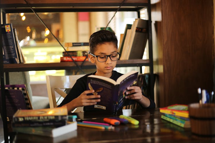 Photograph Of A Kid With Eyeglasses Reading A Book