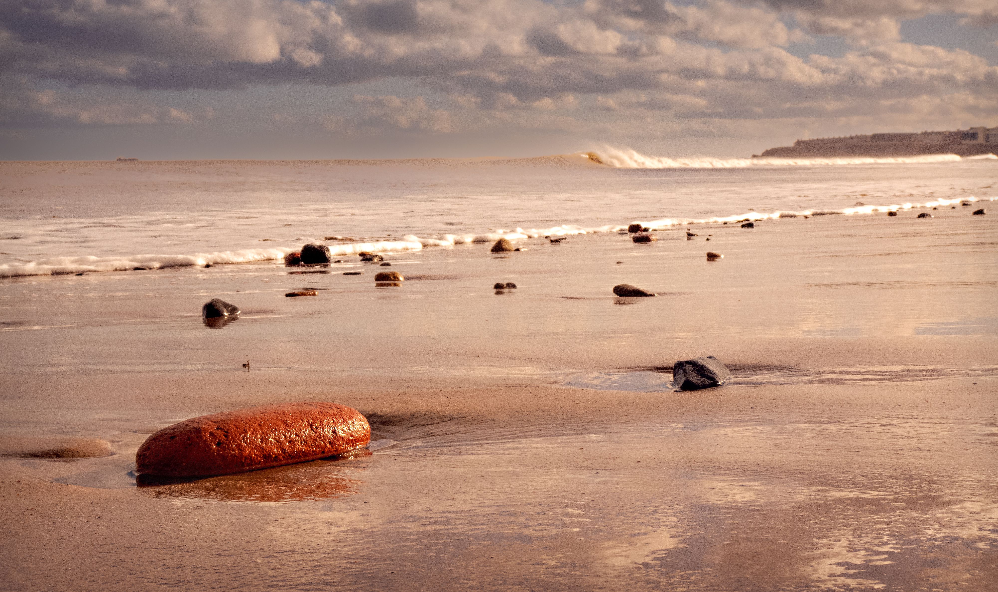 Capture of a serene beach at twilight featuring a rocky shoreline and gentle waves under a cloudy sky.