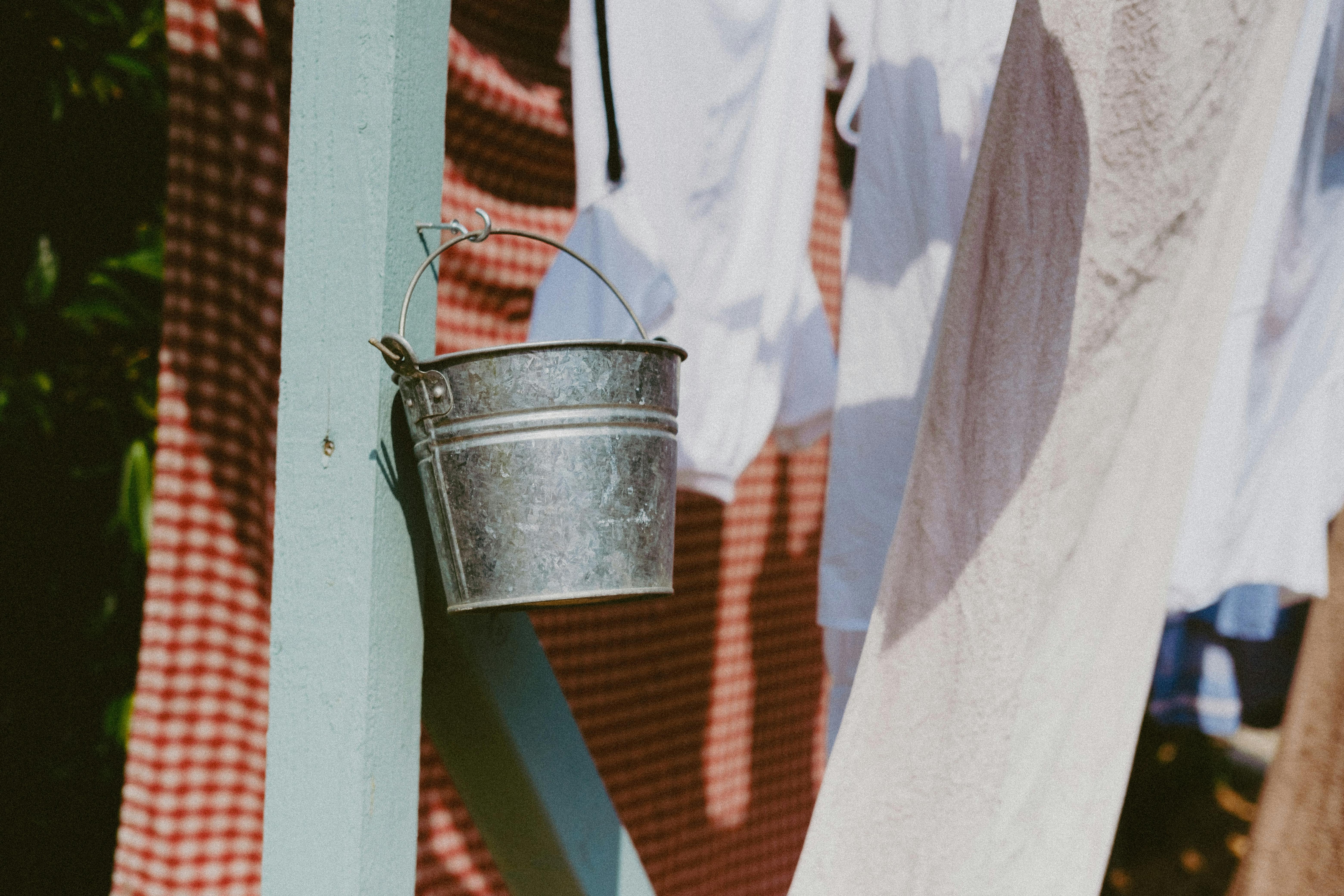 Sunlit scene of clothes drying outdoors with a vintage metal bucket hanging.