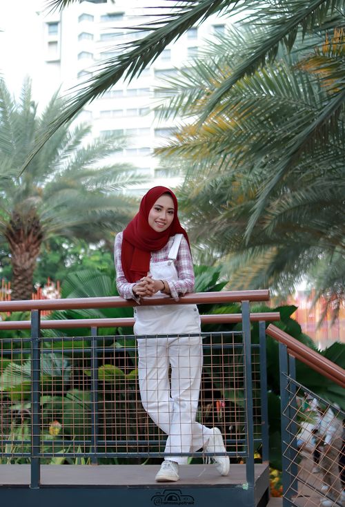 Free Young woman in a red hijab and casual attire smiling on a bridge in Jakarta park. Stock Photo