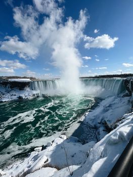 A stunning winter scene of Niagara Falls with cascading water and a blue sky.