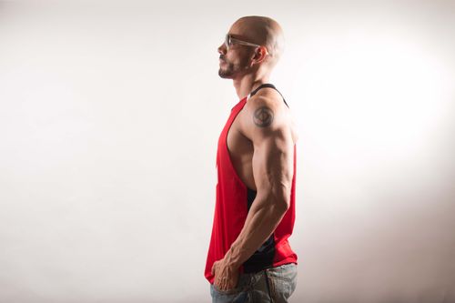 Free Profile of a fit, muscular man wearing a red tank top in a studio setting. Stock Photo