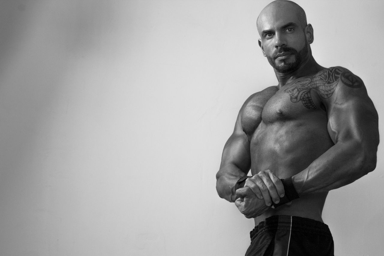 monochrome image of a shirtless bald bodybuilder flexing and posing