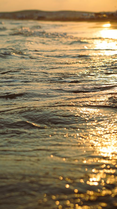 Free A stunning seascape captured at golden hour, showing shimmering ocean waves reflecting the warm sunset light. Stock Photo