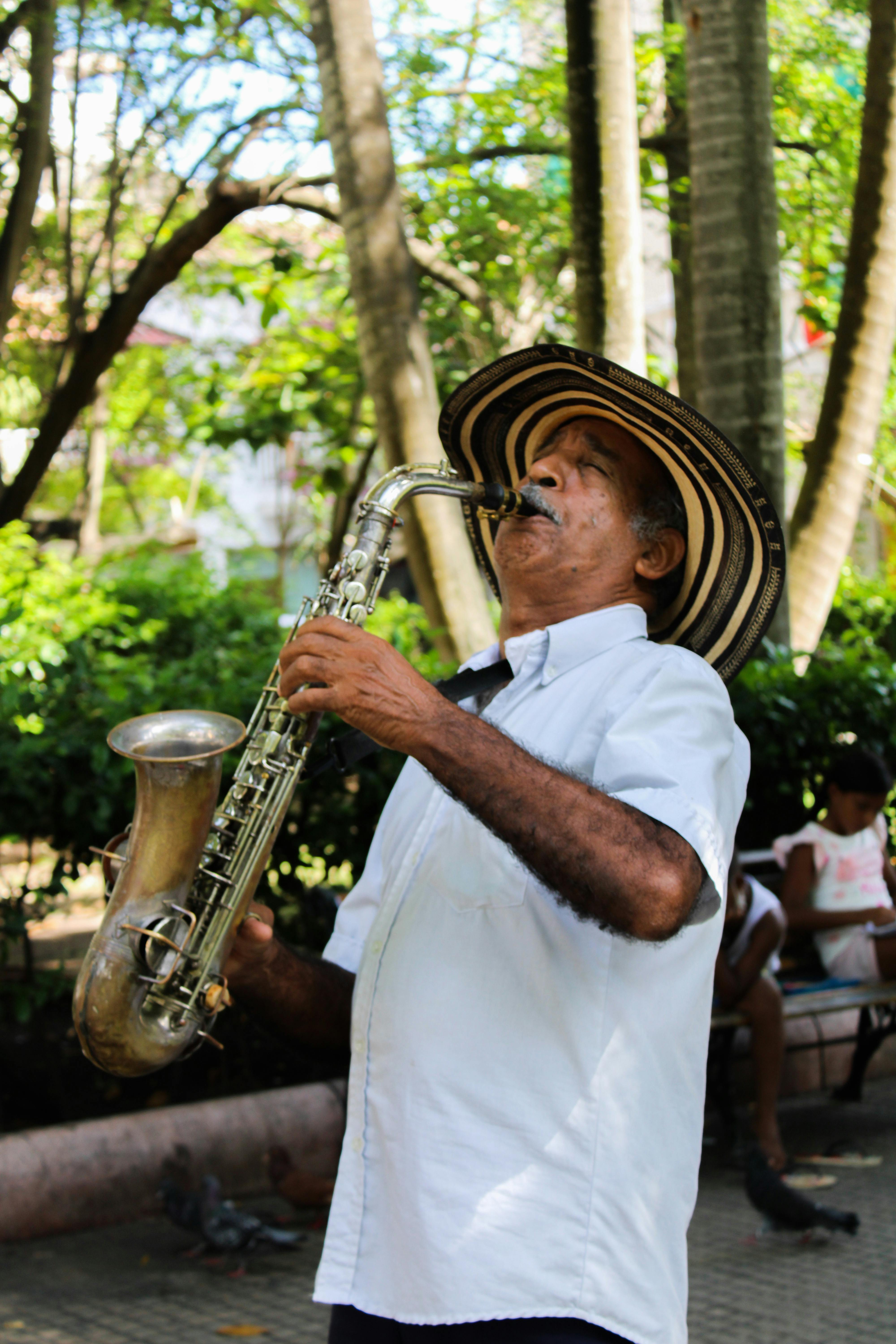 Elderly musician playing saxophone outdoors in Cartagena, showcasing Colombian street culture.