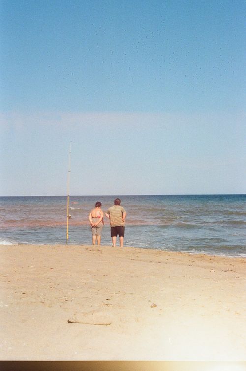 Free A couple enjoys a peaceful day at the beach, admiring the ocean under the blue summer sky. Stock Photo