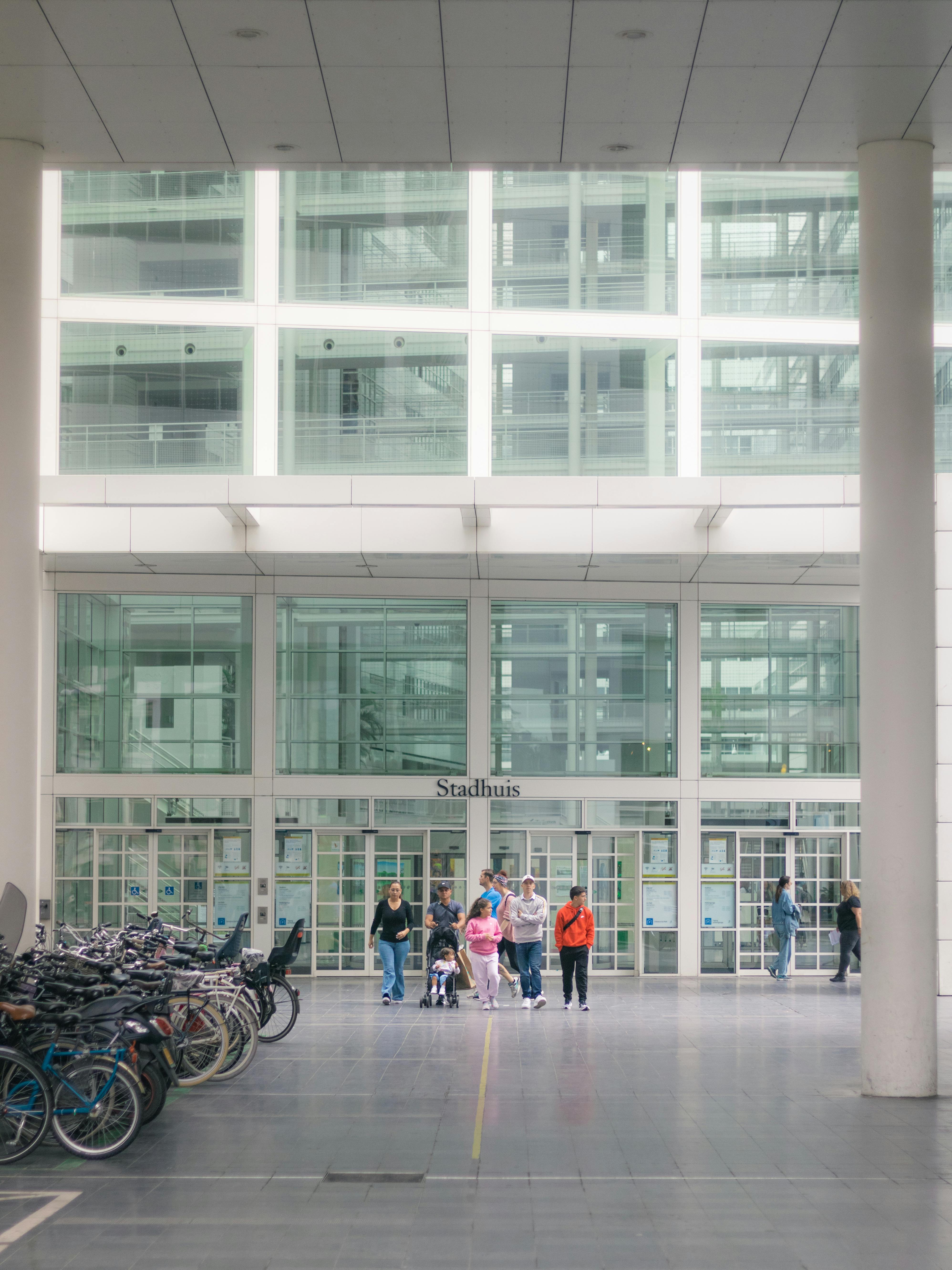 A group of people walking in front of a modern city hall building with bicycles parked nearby.
