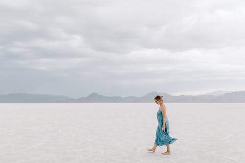 Free A Woman in Blue Dress Walking on White Sand Stock Photo