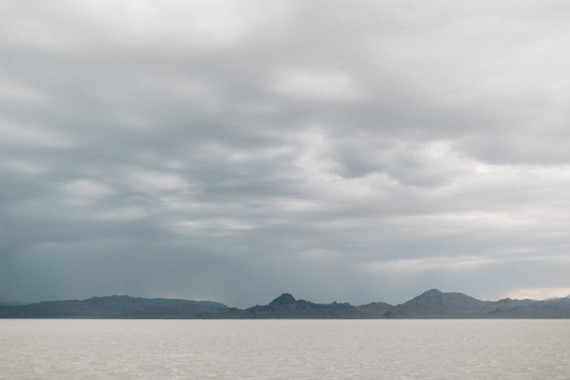 Foto profissional grátis de águas calmas, céu nublado, colinas