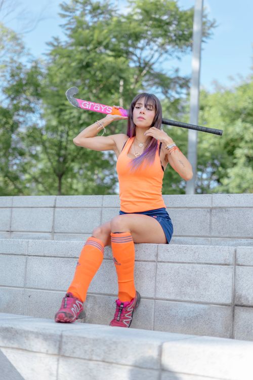 Free Woman in sporty attire poses with a hockey stick on concrete steps in a city park. Stock Photo