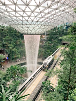 Futuristic indoor waterfall at Jewel Changi Airport, featuring a train passing through lush greenery.