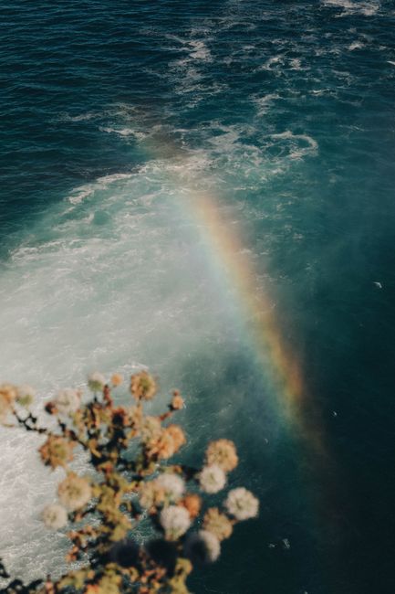 Vibrant rainbow arcs over a cascading waterfall in Antalya, Turkey, with foreground vegetation.