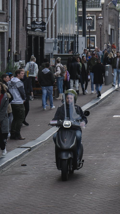 A Man in Black Leather Jacket Riding a Black Motor Scooter
