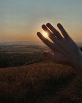 A scenic view of a hand silhouette against a sunset over a grassy field creating a serene atmosphere.