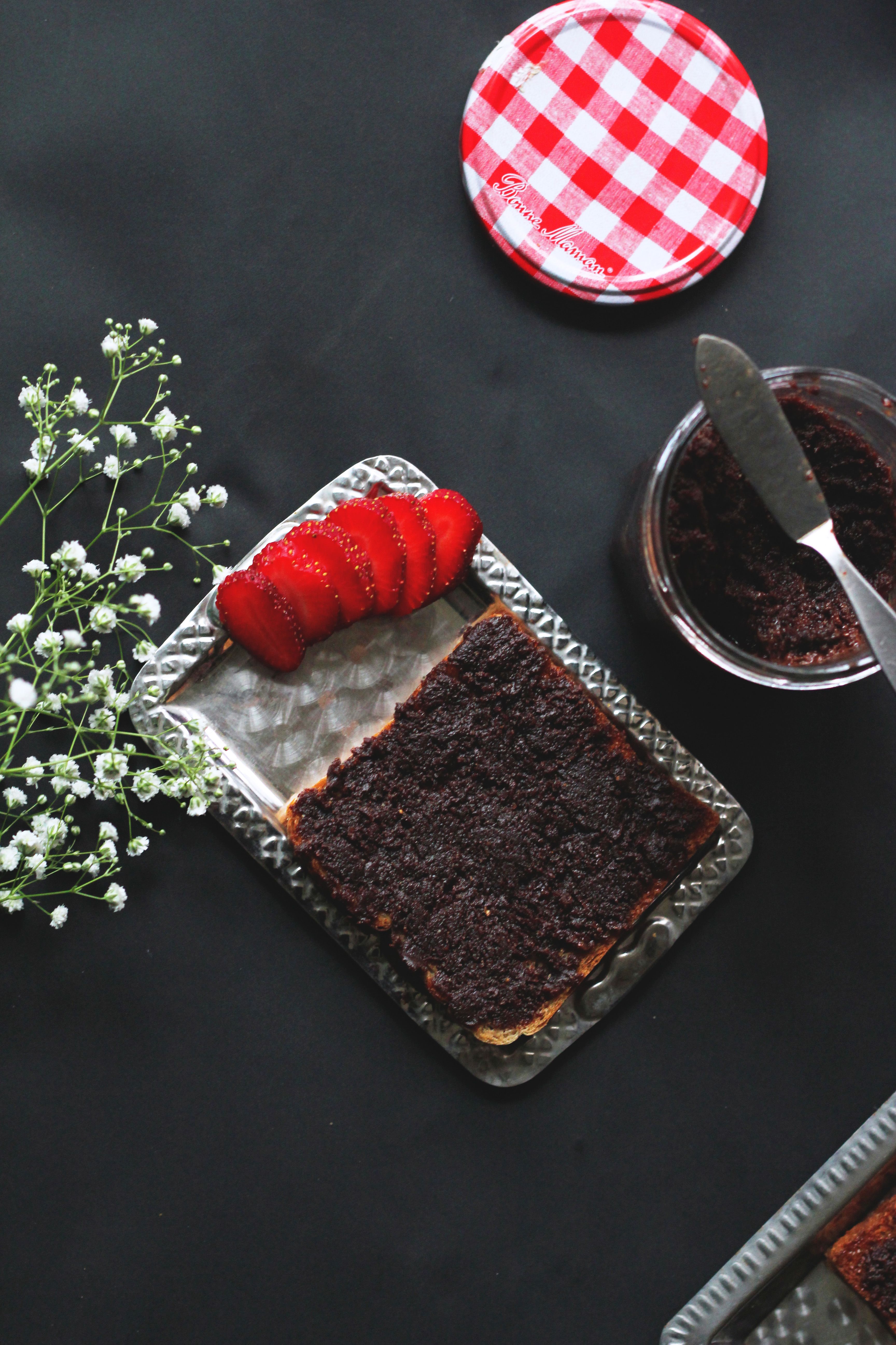 Overhead view of chocolate spread on toast with sliced strawberries on a dark background.