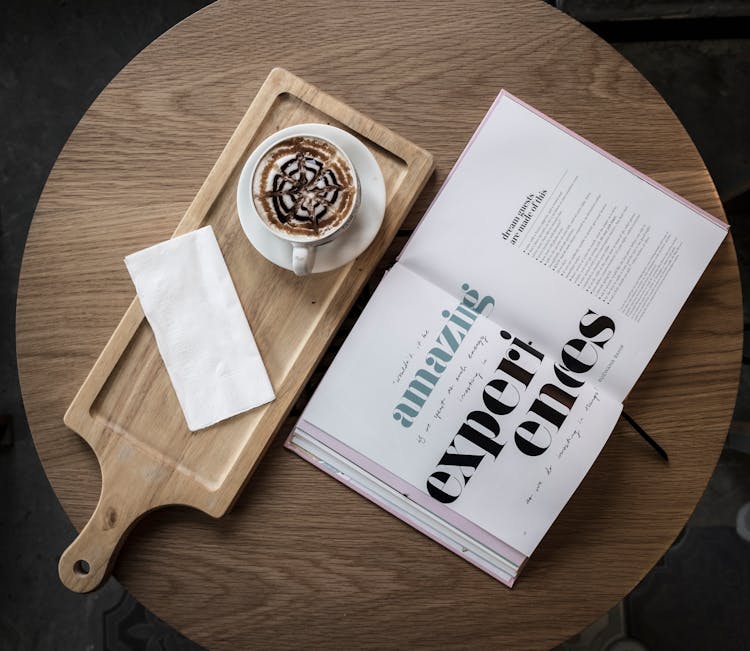 Cappuccino Served On Wooden Board On Table With Open Book