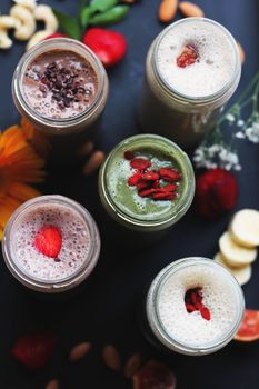 Colorful smoothies with toppings presented in jars on a dark background, highlighting natural ingredients.