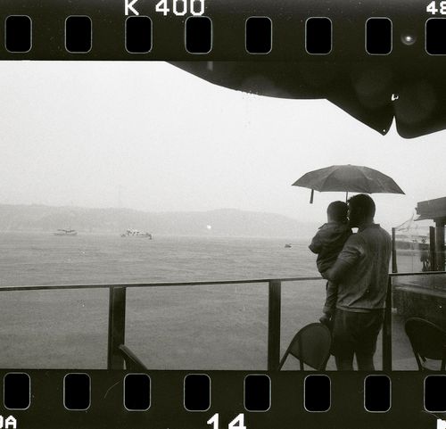 Free A father holds his child under an umbrella by the sea in overcast İstanbul. Stock Photo