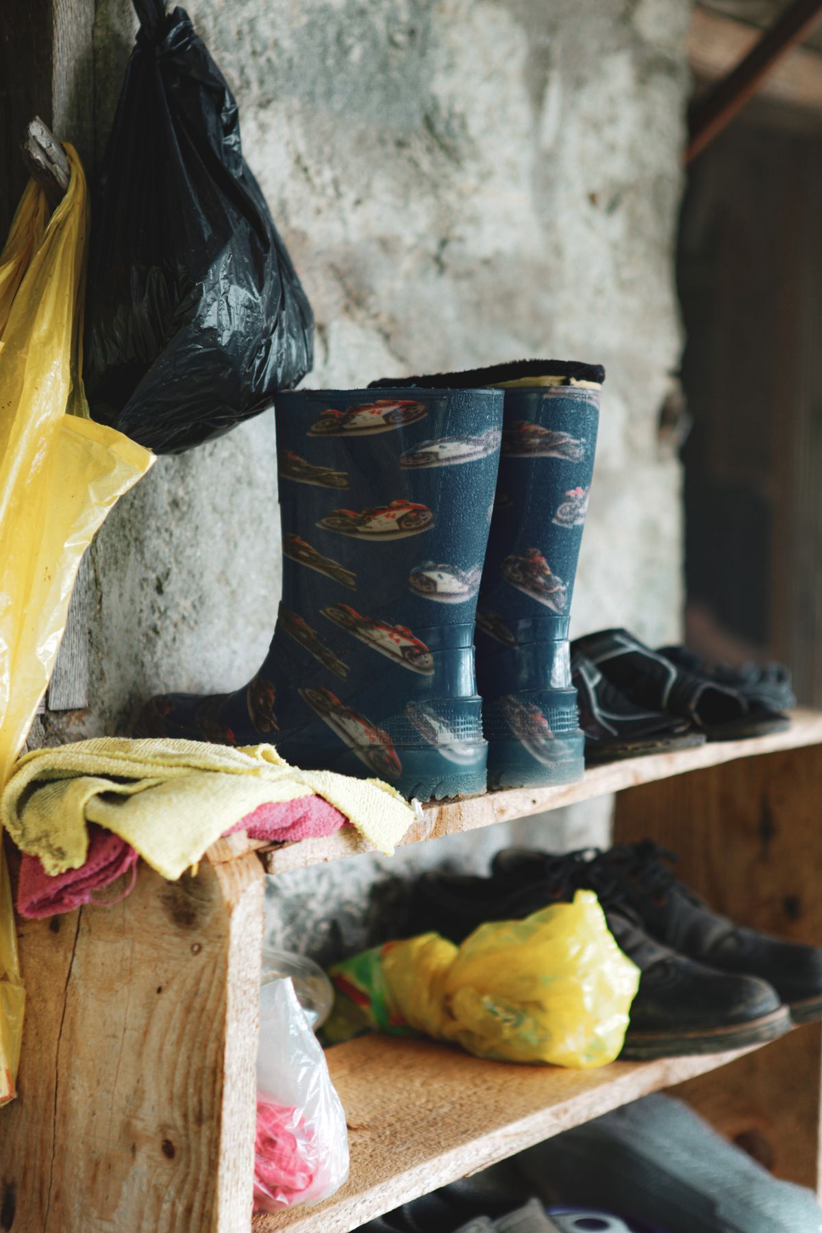 Patterned rain boots displayed on a wooden wall shelf against a rustic stone wall