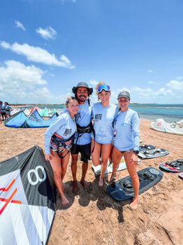 Four friends in matching blue shirts posing with kiteboards on Adicora beach under a sunny sky.