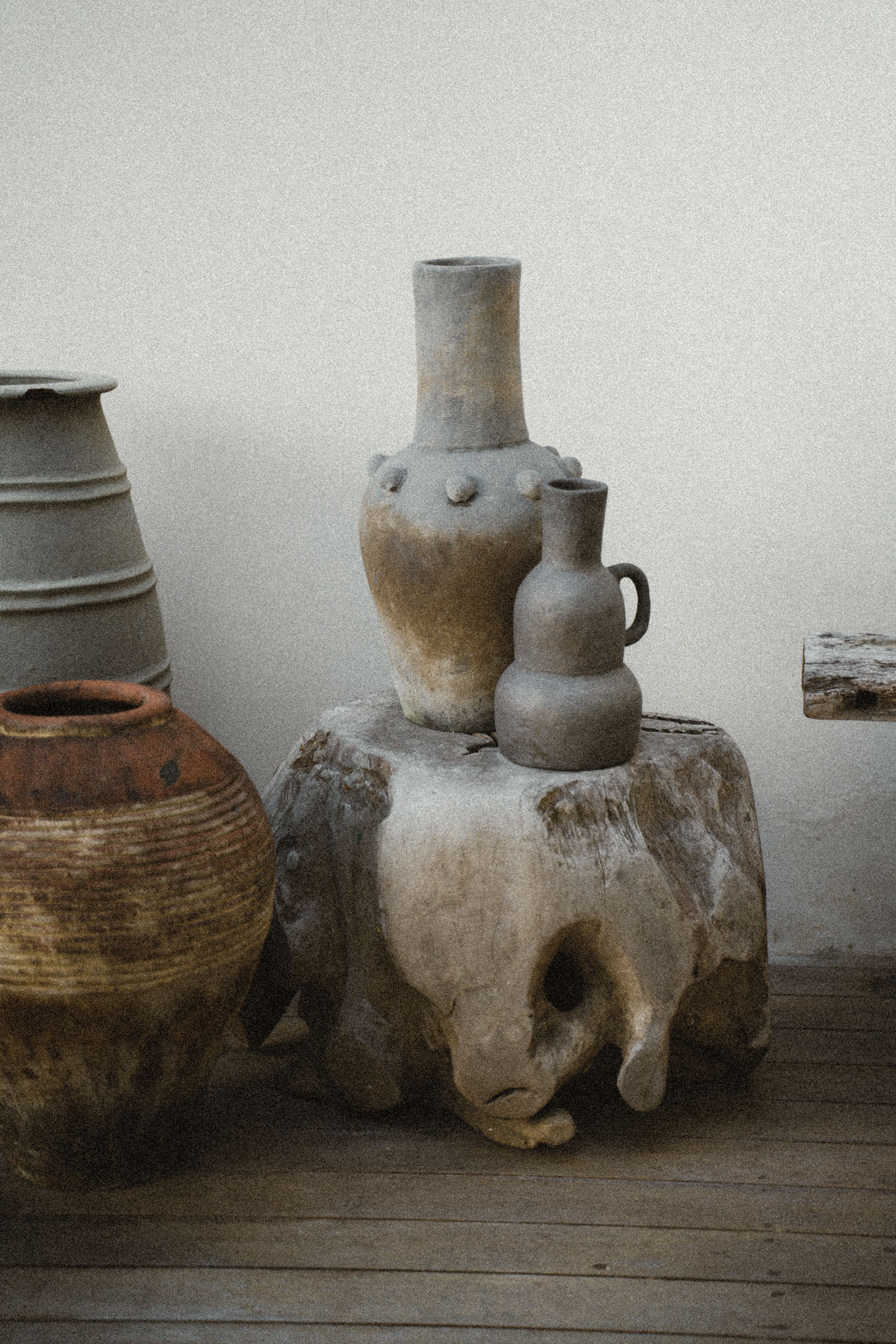 Handmade ceramic pots with rustic finish displayed on a wooden stump in Bali.