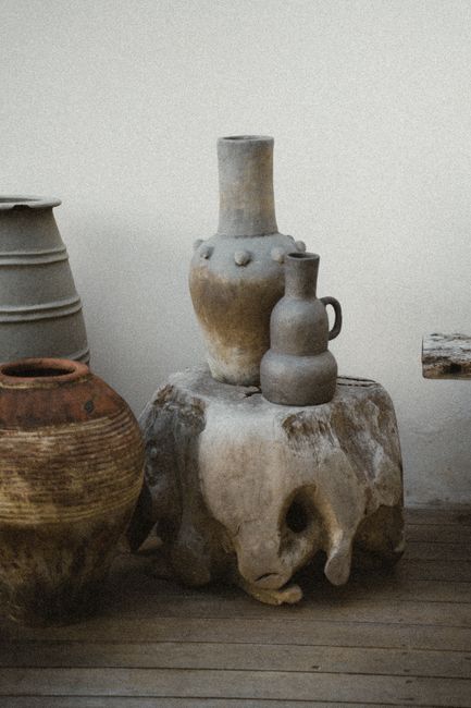 Handmade ceramic pots with rustic finish displayed on a wooden stump in Bali.